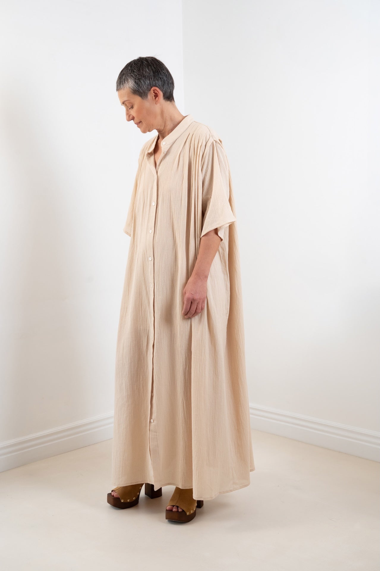 Maxi dress Robe Marine plissée oversize  couleur sable 100% coton, col officier, boutons nacres, vue trois quart, pose dynamique – Onarch
